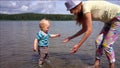 Mom and her little son play and splash around in the clear water of a forest lake on a sunny summer day against a blue sky