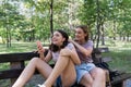 Mom and her teenage daughter have fun laughing on a walk in a summer park. Using a smartphone Royalty Free Stock Photo