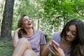 Mom and her teenage daughter have fun laughing on a walk in a summer park. Using a smartphone Royalty Free Stock Photo