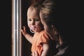 Mom holding a little daughter in her arms in the dark by the window. The baby has a nipple in her mouth. Tinted Royalty Free Stock Photo