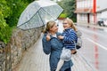 Mom holds her little daughter on hands standing under umbrella. Mother and happy preschool girl, child with eyeglasses Royalty Free Stock Photo