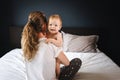 Mom hugs nine-month-old baby girl sitting with her back to camera. Mother with child play together at home sitting on bed Royalty Free Stock Photo