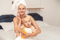 Mom and infant baby in white towels after bathing apply sunscreen or after sun lotion or cream. Children skin care in a hotel or