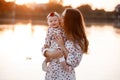 Mom kissing her little daughter near the lake on sunset. The concept of summer holiday. Mother`s, baby`s day. Family spending ti