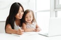 Mom with little cute asian girl using laptop writing notes Royalty Free Stock Photo
