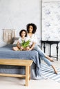 Mom and little cute curly girl sitting on bed with tulips in their hands Royalty Free Stock Photo