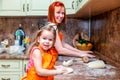 Mom and little cute girl in orange aprons, smiling and making homemade pizza, roll the dough at home in kitchen. Concept happy Royalty Free Stock Photo