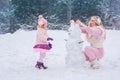 Mom and little daughter dressed in pink clothes have fun and make a snowman in a snowy park