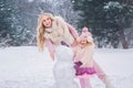 Mom and little daughter dressed in pink clothes have fun and make a snowman in a snowy park