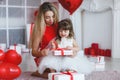 Valentine`s Day - young mother and little daughter in a room on the floor with gifts on a background of red heart-shaped balloons