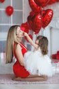 Valentine`s Day - young mother and little daughter in a room on the floor with gifts on a background of red heart-shaped balloons