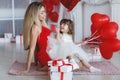 Valentine`s Day - young mother and little daughter in a room on the floor with gifts on a background of red heart-shaped balloons