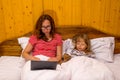 Mom and little daughter lying in bed under a blanket and looking at a laptop Royalty Free Stock Photo