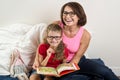 Mom and little daughter read book at home in bed.