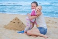 Mom and little girl are building sand castles on the beach. Mom hugs daughter near the sea