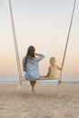 Mom and little girl sit on swing and watch the stunning sunset over the sea. Magical sunrise over sea Royalty Free Stock Photo