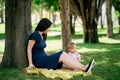 Mom with a little girl are sitting on a blanket on a green lawn under a tree Royalty Free Stock Photo