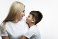 Mom and little son hug and smile. A beautiful blonde and a boy of 7 years old in white T-shirts look at each other. Love and Royalty Free Stock Photo