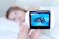 Mom looks at the camera for a little sleeping girl, daughter through the radio, video baby monitor. Protection, care for the