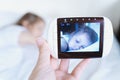 Mom looks at the camera for a little sleeping girl, daughter through the radio, video baby monitor. Protection, care for the