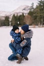 Mom looks at a little boy in her lap while squatting on a snowy lawn