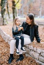 Mom looks at a little girl with an apple in her hands sitting on her lap on a low stone fence in the park Royalty Free Stock Photo