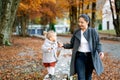 Mom looks at a little girl leading her by the hand along a stone fence in the autumn forest