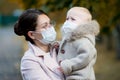 Woman in a medical face mask holds a crying girl in her arms close up