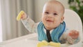 mom Mother feed young baby in white feeding up high chair, first supplement vegetable puree Happy smiling kid eat for Royalty Free Stock Photo