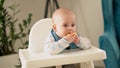 mom Mother feed young baby in white feeding up high chair, first supplement vegetable puree Happy smiling kid eat for Royalty Free Stock Photo