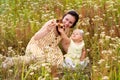 Mom and newborn baby play with a wooden toy biplane among the wildflowers. Portrait of happy mom and newborn daughter in a field