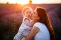 Mom and little daughter enjoy relaxing in a field with lavender at sunset. A beautiful woman with long hair hugs and kiss the baby