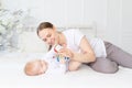 Mom plays with baby rattle on white bed at home