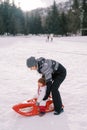 Mom puts a little girl on a sled on a snowy lawn