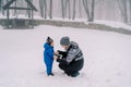 Mom puts on mittens to a little child squatting in a snowy park