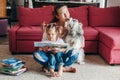 Mom reading book with baby girl toddler at home. Funny home lifestyle family with a licking pet dog. Early age children education