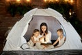 Mom reads children a bedtime story sitting in a tent at home. Mother son and daughter hug and read a book with a flashlight in the Royalty Free Stock Photo