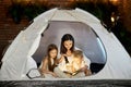 Mom reads children a bedtime story sitting in a tent at home. Mother son and daughter hug and read a book with a flashlight Royalty Free Stock Photo