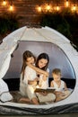 Mom reads children a bedtime story sitting in a tent at home. Mother son and daughter hug and read a book with a flashlight Royalty Free Stock Photo