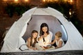 Mom reads children a bedtime story sitting in a tent at home. Mother son and daughter hug and read a book with a flashlight in Royalty Free Stock Photo