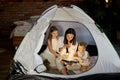 Mom reads children a bedtime story sitting in a tent at home. Mother son and daughter hug and read a book with a flashlight in Royalty Free Stock Photo
