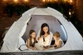 Mom reads children a bedtime story sitting in a tent at home. Mother son and daughter hug and read a book with a flashlight in Royalty Free Stock Photo