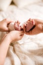 Mom`s and father hands are holding little cute legs of a newborn baby at home on a white bed. Royalty Free Stock Photo