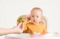 Mom`s hand with a boiled head of broccoli. The baby is surprised by unfamiliar food. Selective focus Royalty Free Stock Photo