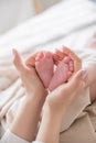 Mom`s hands are holding little cute legs of a newborn baby at home on a white bed Royalty Free Stock Photo