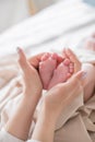 Mom`s hands are holding little cute legs of a newborn baby at home on a white bed Royalty Free Stock Photo