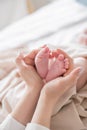 Mom`s hands are holding little cute legs of a newborn baby at home on a white bed Royalty Free Stock Photo