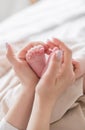 Mom`s hands are holding little cute legs of a newborn baby at home on a white bed Royalty Free Stock Photo