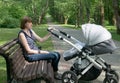 mom sits on a bench and rolls a baby carriage