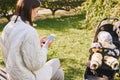 Mom sits with a phone on a bench near a stroller with a baby in the park Royalty Free Stock Photo